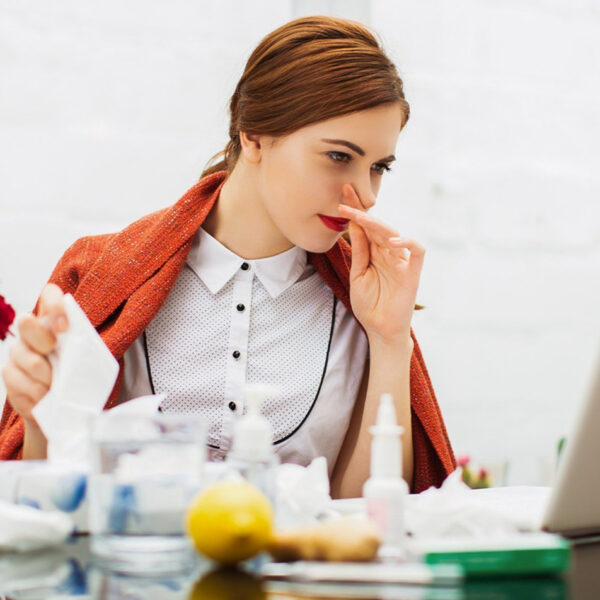 Serganti peršalusi moteris biure.